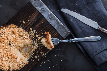 Plum cake on a wooden tray, a piece of cake on a fork,  on a dark metallic background top view.