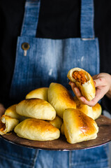 Traditional homemade baked patties or pies with potatoes and cabbage. Baked russian pies made of yeast dough in a rustic style. A woman in a blue apron holds pies in her hands.