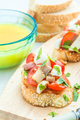 Bruschetta with tomato, bacon, matsarela and parsley on a wooden plate, a cup of orange juice on a blue tablecloth. Close-up. Italian appetizer.