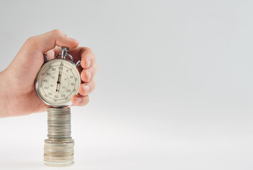 time is money. hand holding a stopwatch on a stack of silver coins