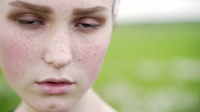 Close up portrait of beautiful young girl with freckles, green eyes and red rose cheeks wearing black t-shirt looking on camera. Sad brunette teenager with dark expressive eyebrows on green background
