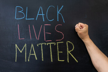 Fototapeta premium the text Black lives matter, on a chalkboard. A man's fist against a chalkboard