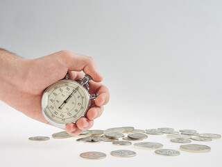 time is money. hand holding a stopwatch on a background of silver coins