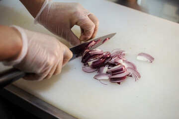 Chef thinly slices purple onion on the white background. Cook's hands are in gloves. Preparing food in the restaurant. 