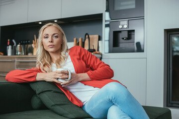 Obraz premium serious woman looking at camera while sitting on sofa with cup of tea