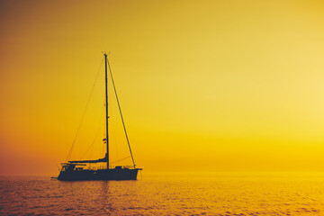 Silhouette of a sailing boat in sunset / sunrise time and ocean horizon.