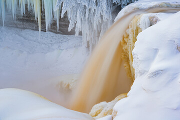 Winter landscape of Upper Tahquamenon Falls captured with motion blur and framed by icicles, snow, and conifers, Michigan's Upper Peninsula, USA