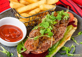 A serving of Steak Sandwich with Beetroot, Lettuce and a side of French Fries and Tomato Sauce