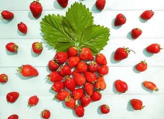 Composition of a big figure strawberry is laid out of strawberries with green leaf. Ripe red strawberries on a blue wooden background. Freshly berries, sunny summer day. Top view, close up, copy space