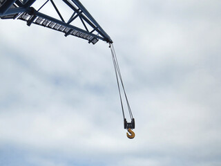 Close up of hanging crane hook and white cloudy sky. Industrial scene.Tall crane boom at construction site.