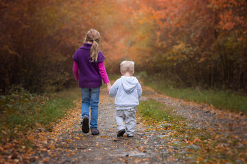 Naklejka na ściany i meble Two siblings wolking in autumn nature, little brother with sister going on path
