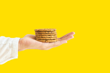 Young woman holds in stretched out hand stack of homemade chocolate chip cookies with nuts on bright yellow background. Baking american traditional pastry concept