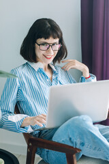 Beautiful brunette with a short haircut works in the home office on a blue background. Typing on a laptop, calling on the phone, transferring documents, making notes, drinking coffee from a mug.