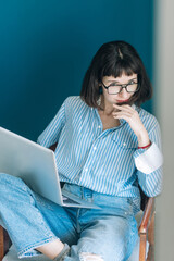 Beautiful brunette with a short haircut works in the home office on a blue background. Typing on a laptop, calling on the phone, transferring documents, making notes, drinking coffee from a mug.