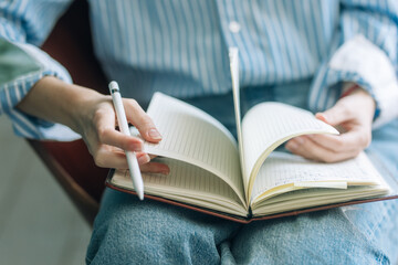Beautiful brunette with a short haircut works in the home office on a blue background. Typing on a laptop, calling on the phone, transferring documents, making notes, drinking coffee from a mug.