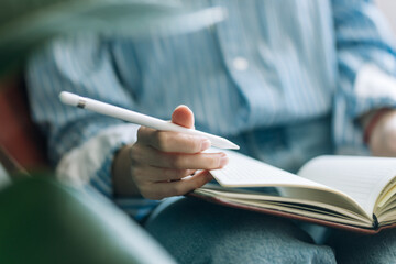 Beautiful brunette with a short haircut works in the home office on a blue background. Typing on a laptop, calling on the phone, transferring documents, making notes, drinking coffee from a mug.
