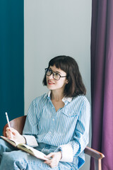 Beautiful brunette with a short haircut works in the home office on a blue background. Typing on a laptop, calling on the phone, transferring documents, making notes, drinking coffee from a mug.