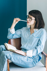 Beautiful brunette with a short haircut works in the home office on a blue background. Typing on a laptop, calling on the phone, transferring documents, making notes, drinking coffee from a mug.