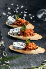 Italian cuisine, antipasti and tapas. Bruschetta of baguette and cottage cheese, tomato, salmon capers, pesto. Serving dishes in a restaurant in white plate.