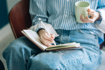 Beautiful brunette with a short haircut works in the home office on a blue background. Typing on a laptop, calling on the phone, transferring documents, making notes, drinking coffee from a mug.