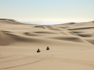 Fototapeta na wymiar Quad driving people - two happy bikers in sand desert dunes at ocean coast beach, Africa, Namibia, Namib, Walvis Bay, Swakopmund.
