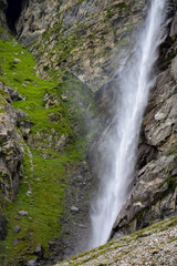 Obraz premium Stunning landscape at roaring Vasudhara falls, people enjoying the fall, big rocky mountains and clouds. Monsoon trek taken in August starts near Mana (last indian village) in Uttarakhand India.