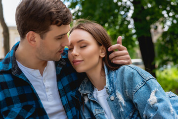 handsome man touching hair of attractive girlfriend with closed eyes