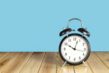 black retro alarm clock with bells on wood table with blue background, showing ten o'clock..