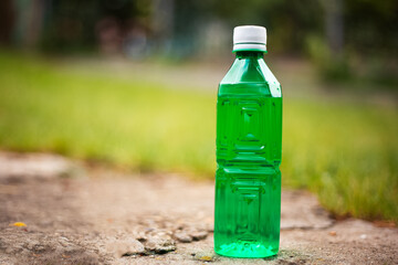 Close-up of green plastic bottle on blurred outdoors background.