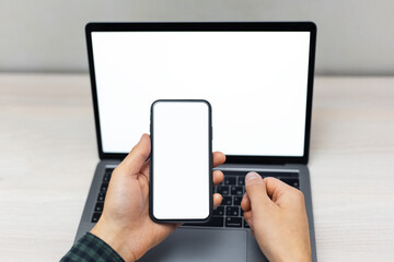 Top view of male hands holding smartphone with mockup on screen beside laptop. background of wooden table.