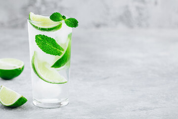 Mojito cocktail with ice, fresh mint and lime in glass on gray stone background.