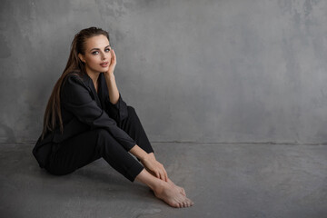 model girl in a black suit on a background of a gray wall