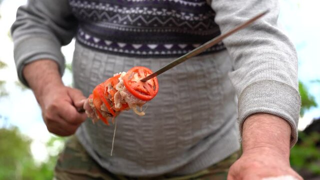 Mature man impales raw shashlik on skewer. Close up of men's hands hold skewer with barbecue. Concept of picnic outdoor.