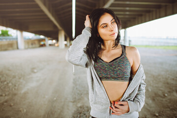 Beautiful young fit woman in sportswear posing with urban view under a bridge. Beauty and sport concept