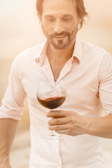 Handsome man going to taste luxury red wine. Winemaker smiles looking for drink in wineglass while standing on the coast. Toned image.
