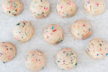 Birthday cake sprinkled edible cookie dough balls on white parchment paper.