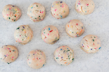 Birthday cake sprinkled edible cookie dough balls on white parchment paper.