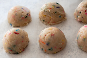 Birthday cake sprinkled edible cookie dough balls on white parchment paper.