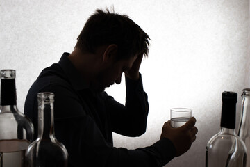A man and a glass of vodka. Alcoholism, alcohol addiction, delirium tremens. 
Silhouette photo.
