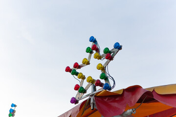 Illumination at carousel roof. Star-shaped lamp with multi-colored light bulbs on sky background on sunny day.