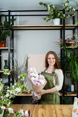 Beautiful florist girl with red hair and a beautiful bouquet of roses at the counter in a flower shop. Sale of flowers and plants