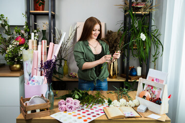 A girl florist with red hair collects a bouquet of roses in a flower shop. Remote workshop for the Assembly of bouquets.