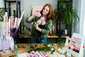 A girl florist with red hair collects a bouquet of roses in a flower shop. Remote workshop for the Assembly of bouquets.