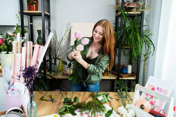 A girl florist with red hair collects a bouquet of roses in a flower shop. Remote workshop for the Assembly of bouquets.