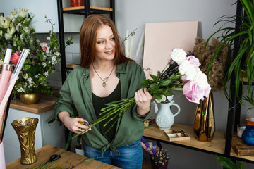 A girl florist with red hair collects a bouquet of roses in a flower shop. Remote workshop for the Assembly of bouquets.