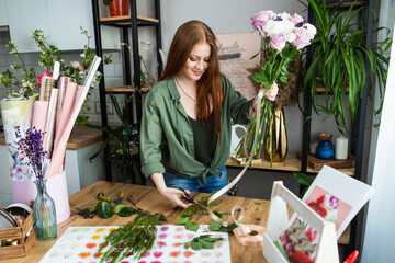 A girl florist with red hair collects a bouquet of roses in a flower shop. Remote workshop for the Assembly of bouquets.