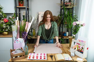 A girl florist with red hair collects a bouquet of roses in a flower shop. Remote workshop for the Assembly of bouquets.