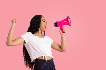 Portrait of a young woman being loud and heard by shouting through megaphone with fist up and mouth...
