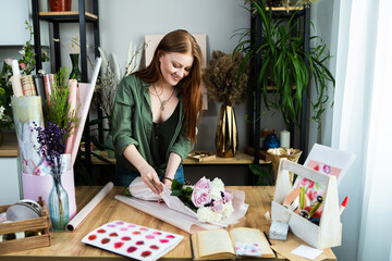 A girl florist with red hair collects a bouquet of roses in a flower shop. Remote workshop for the Assembly of bouquets.