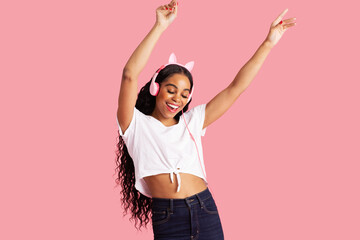 Portrait of an excited smiling young woman dancing with headphones against pink studio background